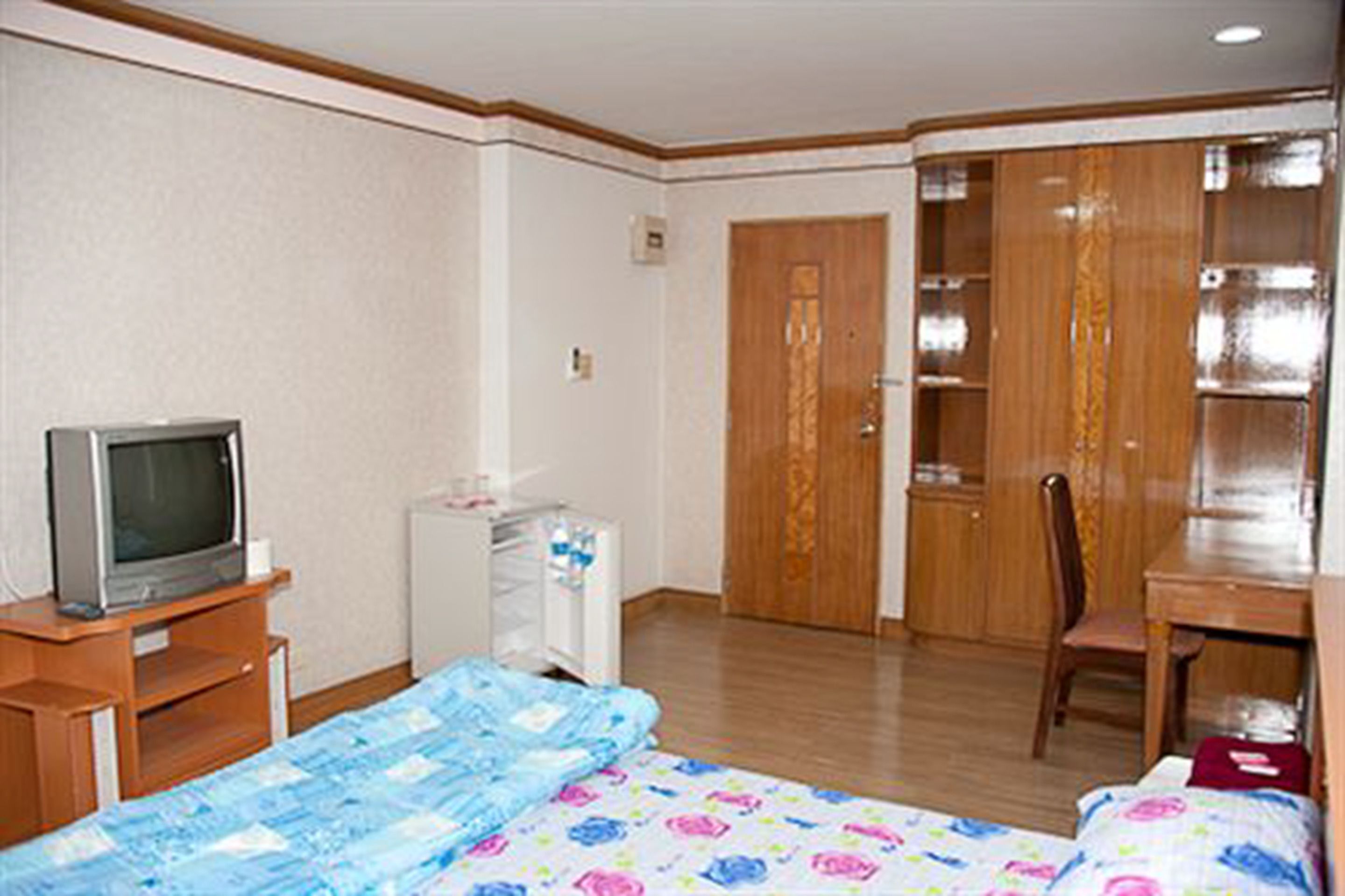 A hotel room with a bed, a desk, a chair, a television, and a wardrobe.