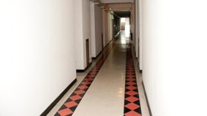 En lång, smal hall med vita väggar och ett svart- och rödrandigt golv.