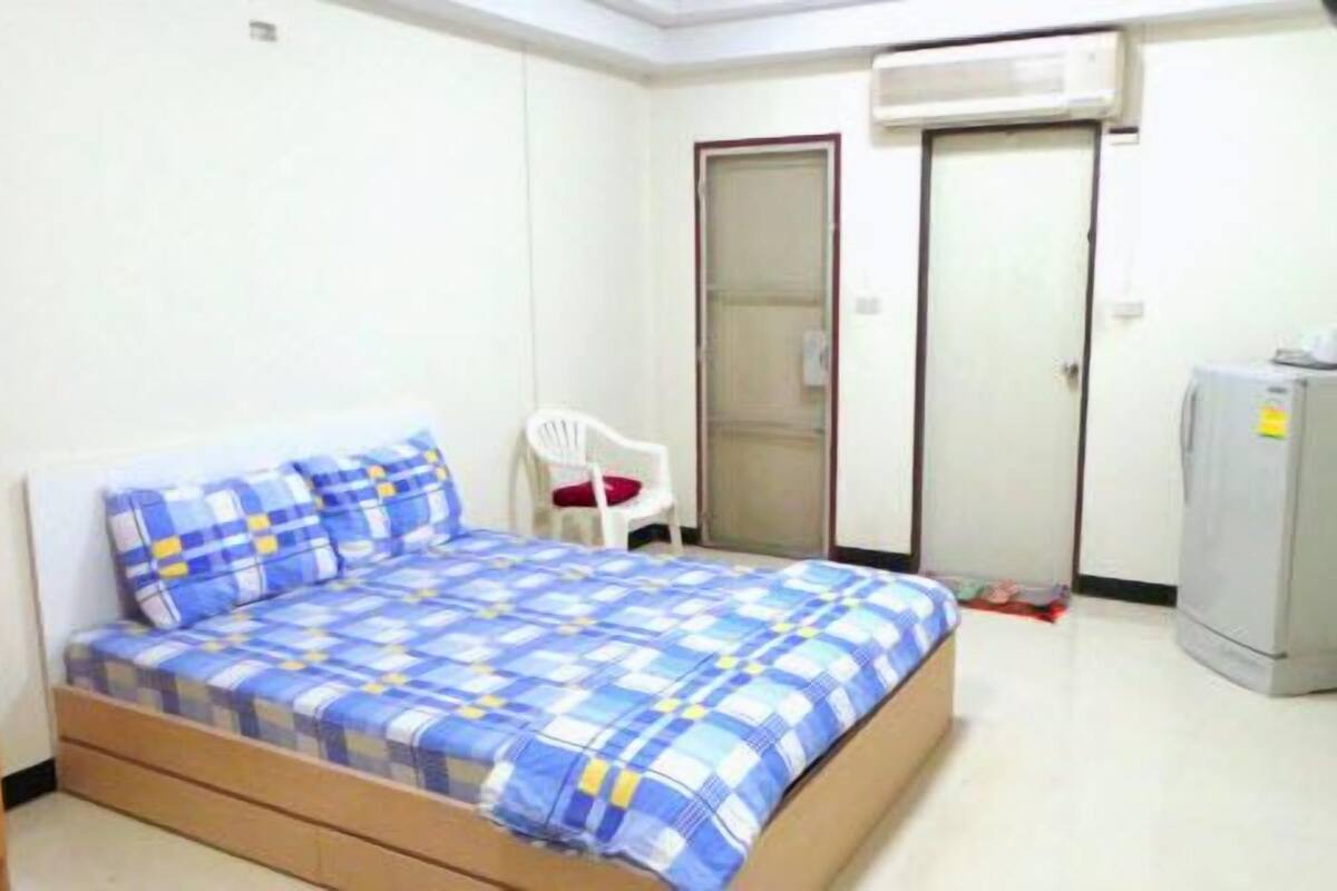 Ein Schlafzimmer mit einem Bett, einem weißen Stuhl, einem Kleiderschrank und einem Kühlschrank.