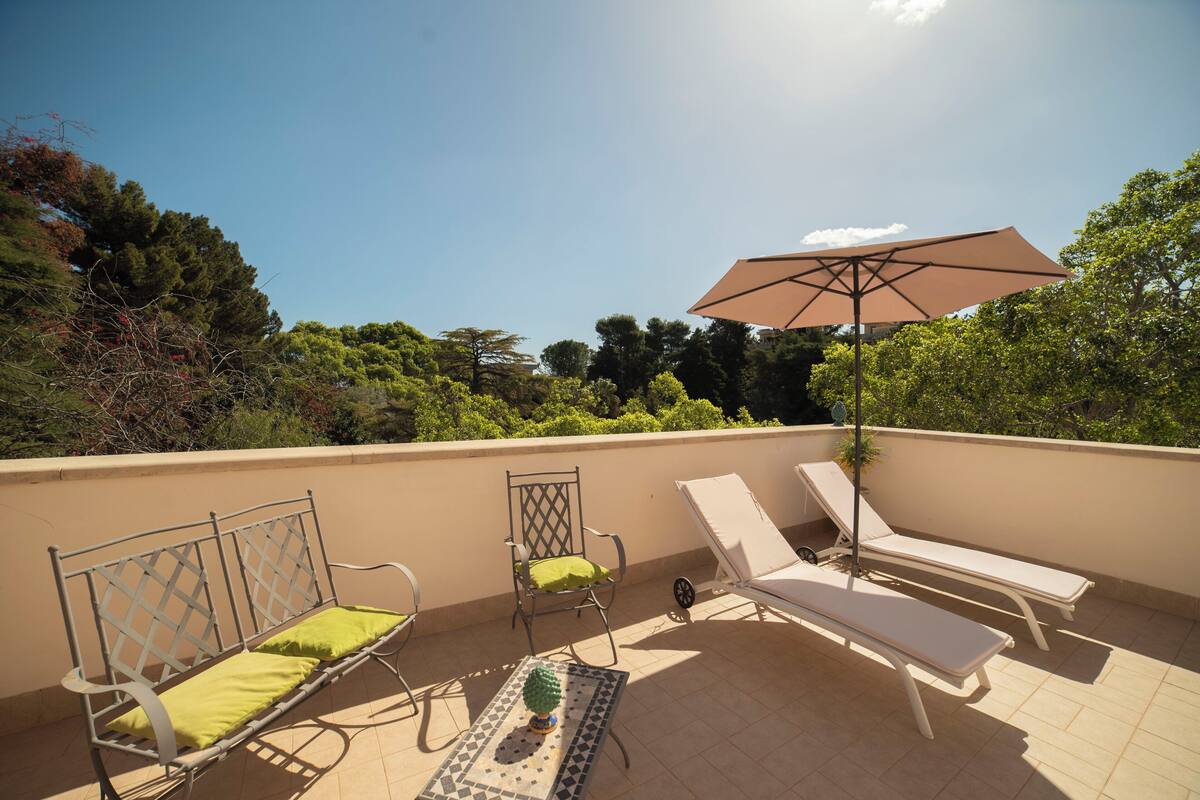 A rooftop terrace with a metal bench, a lounge chair, a dining table, and a large umbrella.