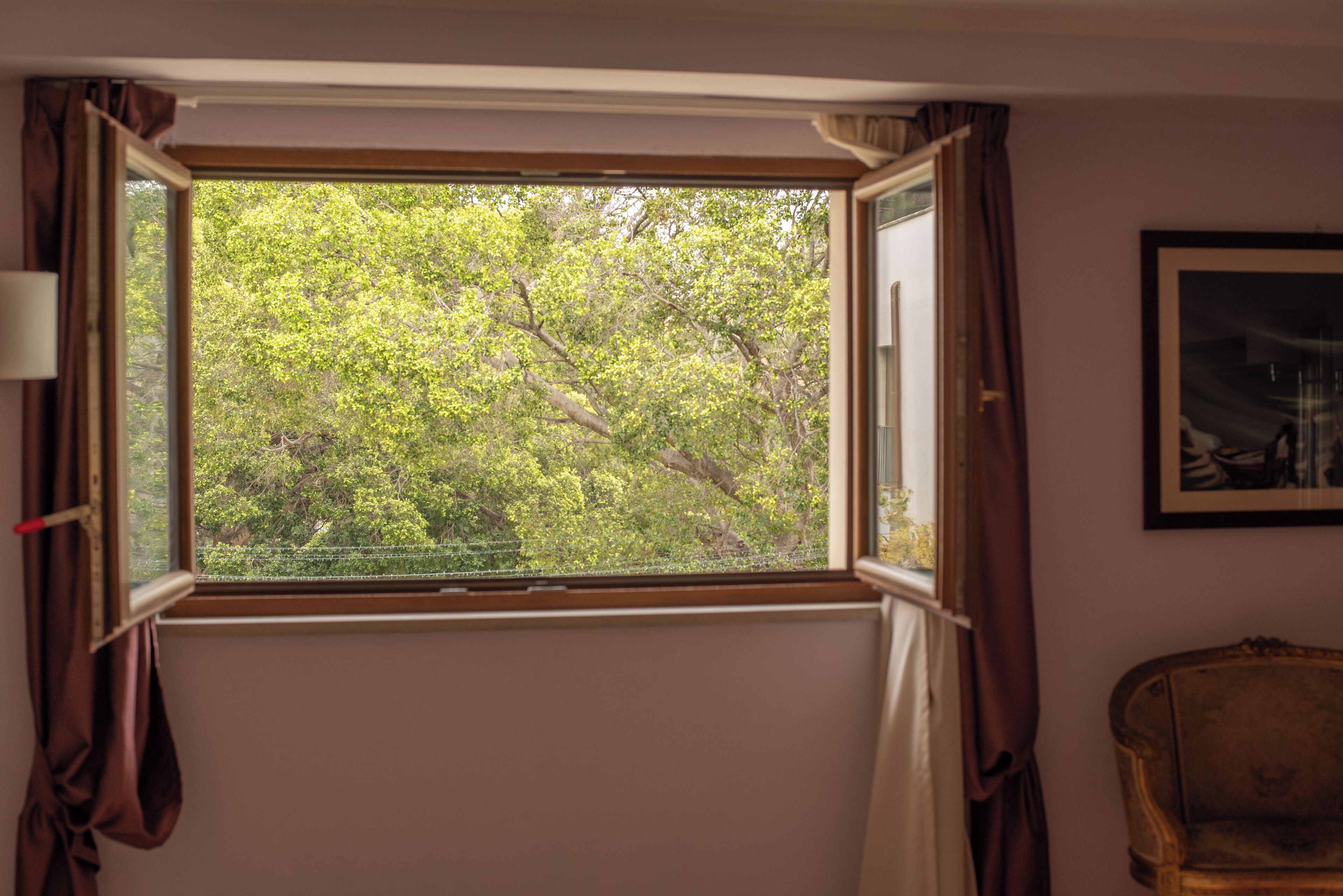 Ein Zimmer mit Fenster, Vorhängen, einem gerahmten Bild an der Wand und einem Sessel.
