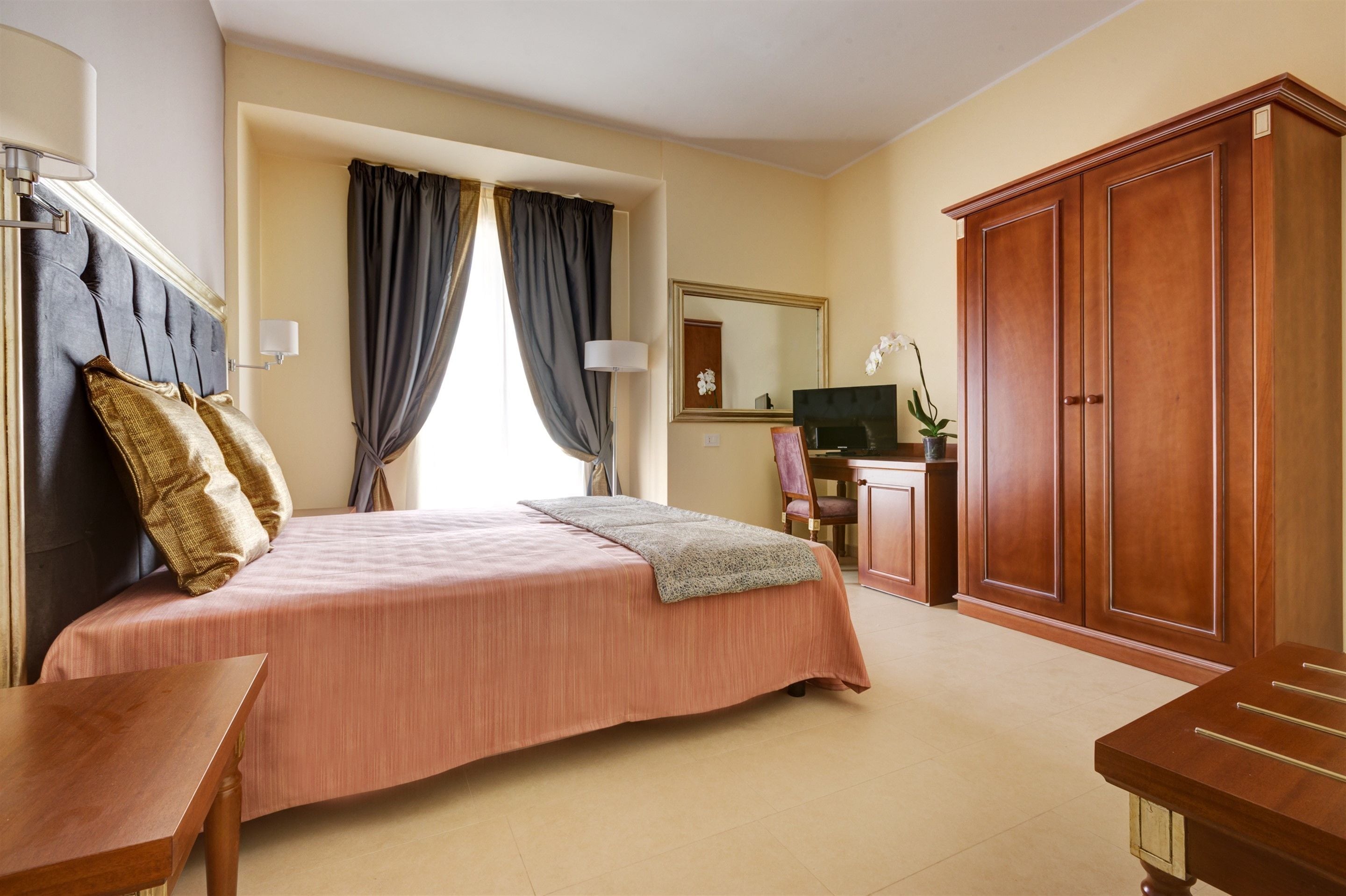 A hotel room with a bed, a desk, a wardrobe, and a mirror.