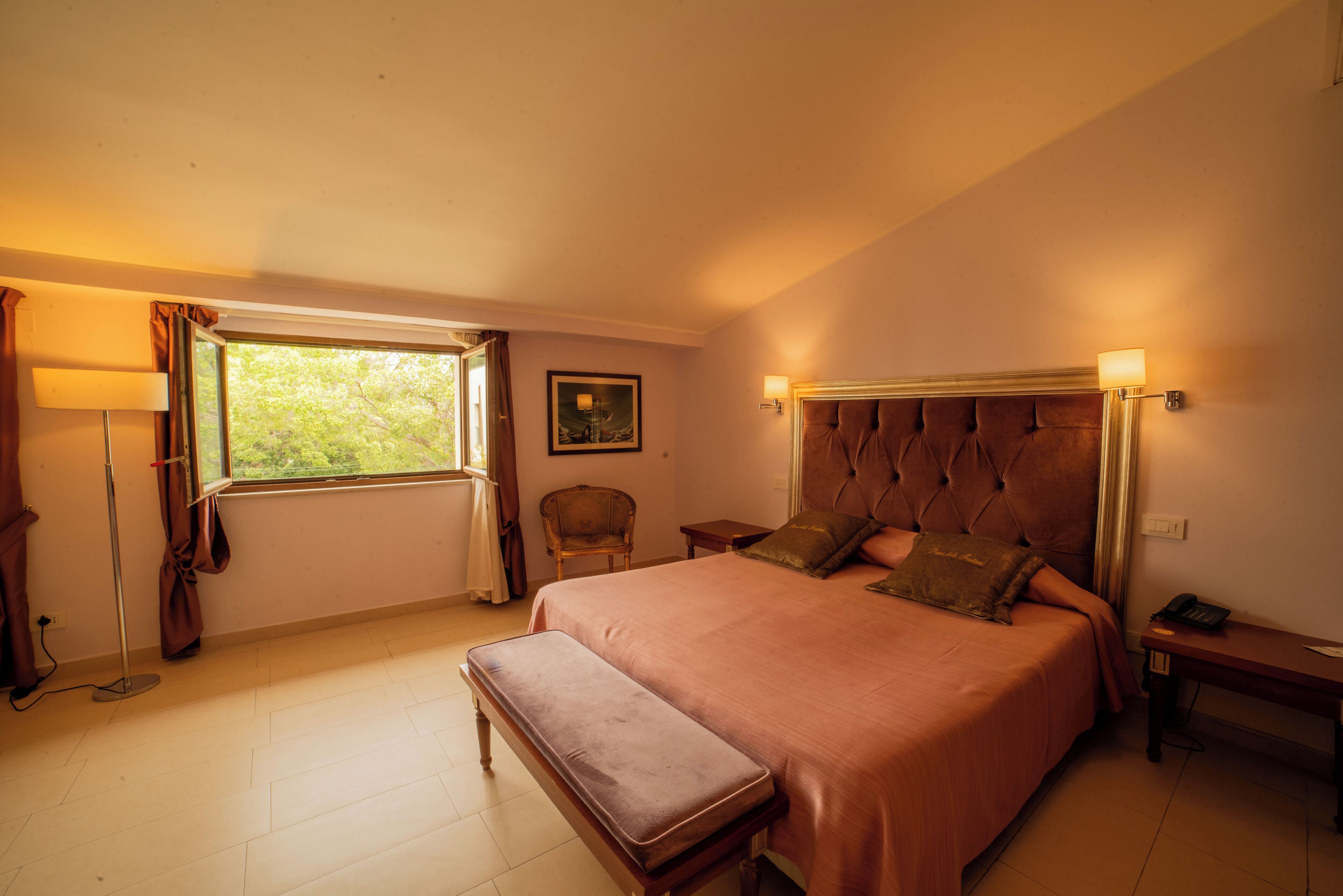 Un dormitorio con una cama grande, una mesita de noche, una lámpara, una silla y una ventana con cortinas.