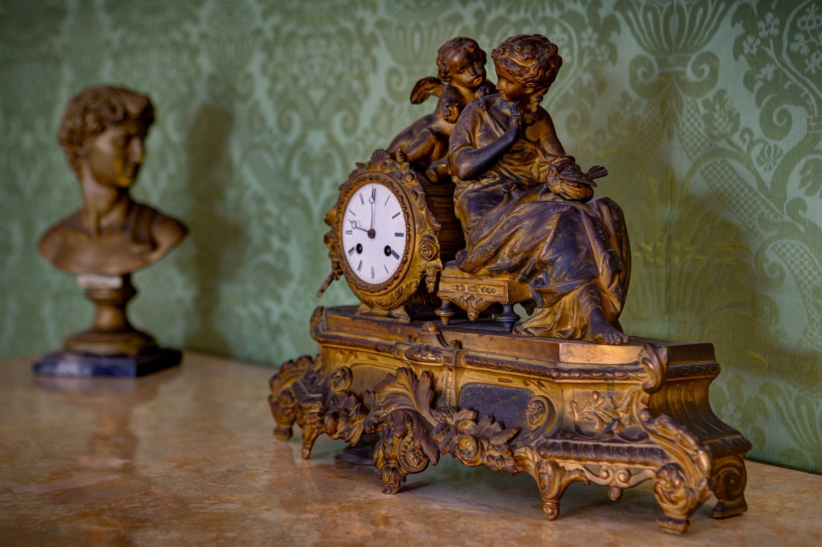 A detailed clock with intricate carvings and a bust sculpture on a table.