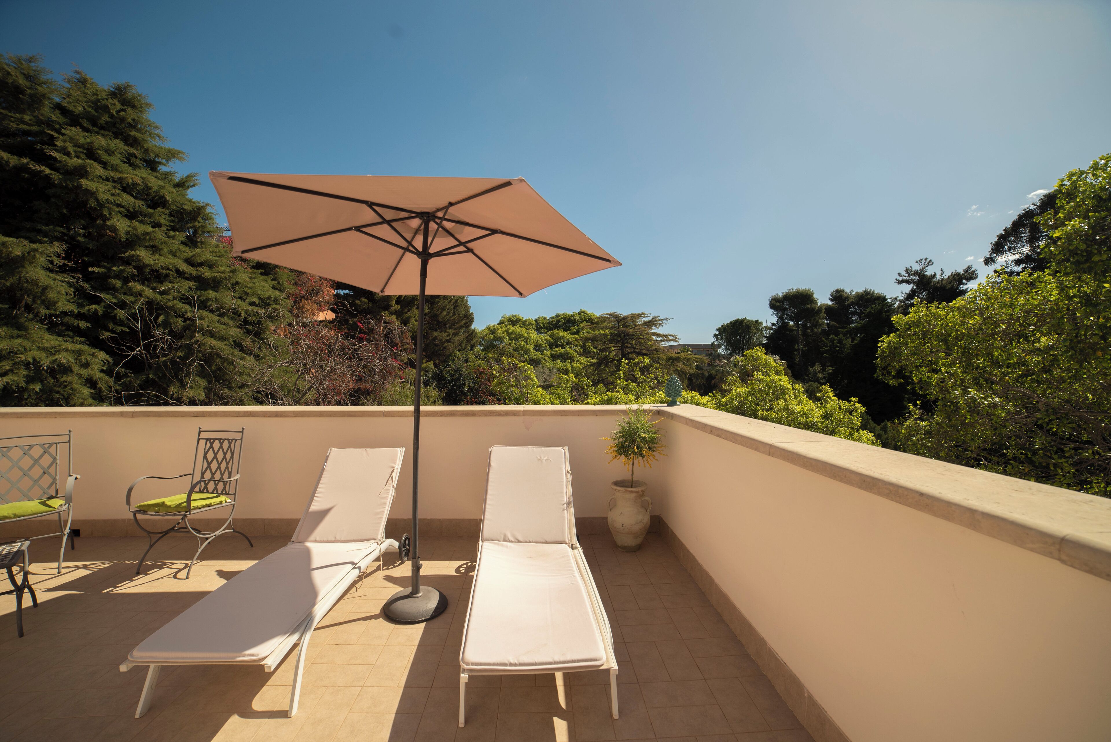 Terraza en la azotea con dos tumbonas, una mesa y una sombrilla.