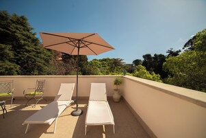 Terraza en la azotea con dos tumbonas, una mesa y una sombrilla.