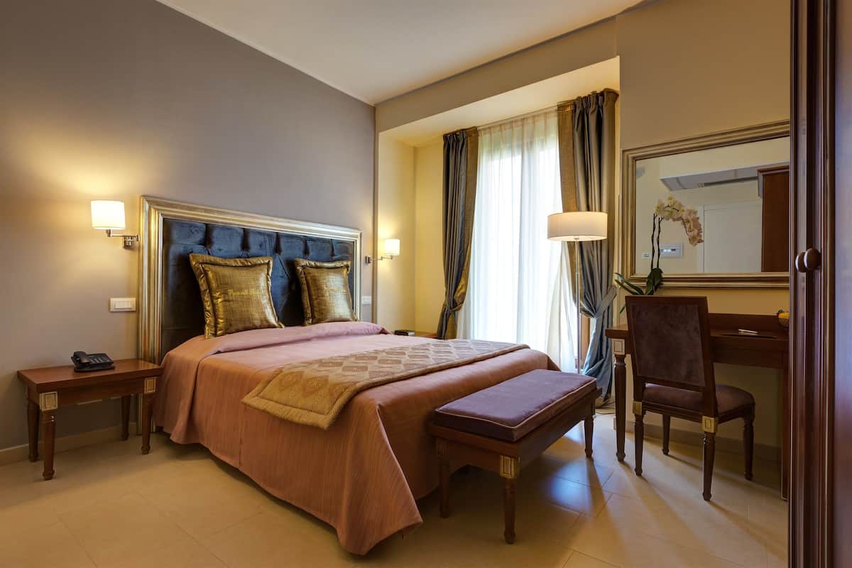 A hotel room with a large bed, bedside tables, a desk, and a chair.