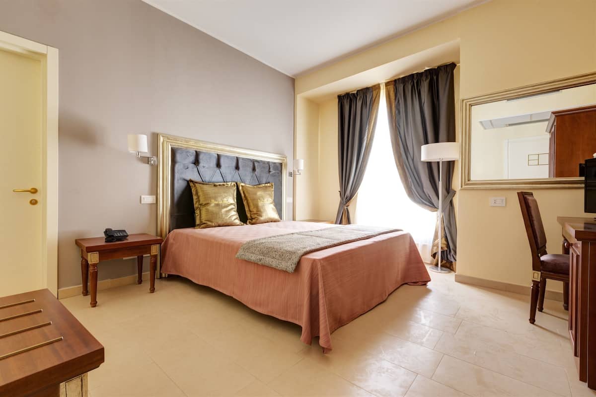 A hotel room with a bed, bedside table, lamp, chair, and a mirror on the wall.