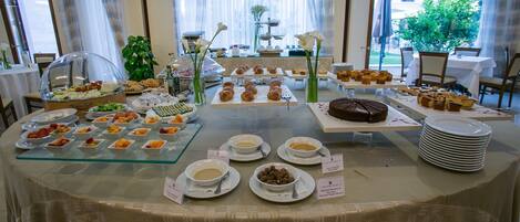 A buffet table with various food items and dishes, including bowls of soup and pastries, arranged on a table with a patterned tablecloth.