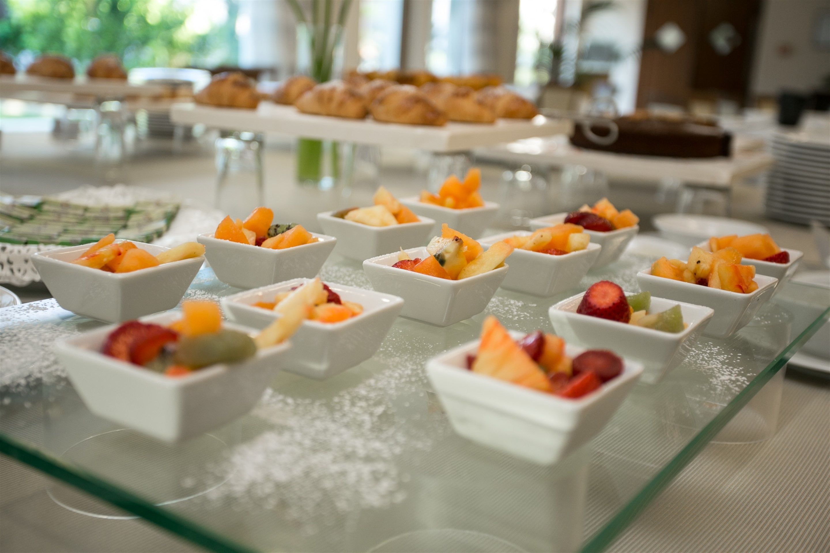 A buffet with various fruit bowls arranged on a glass table.