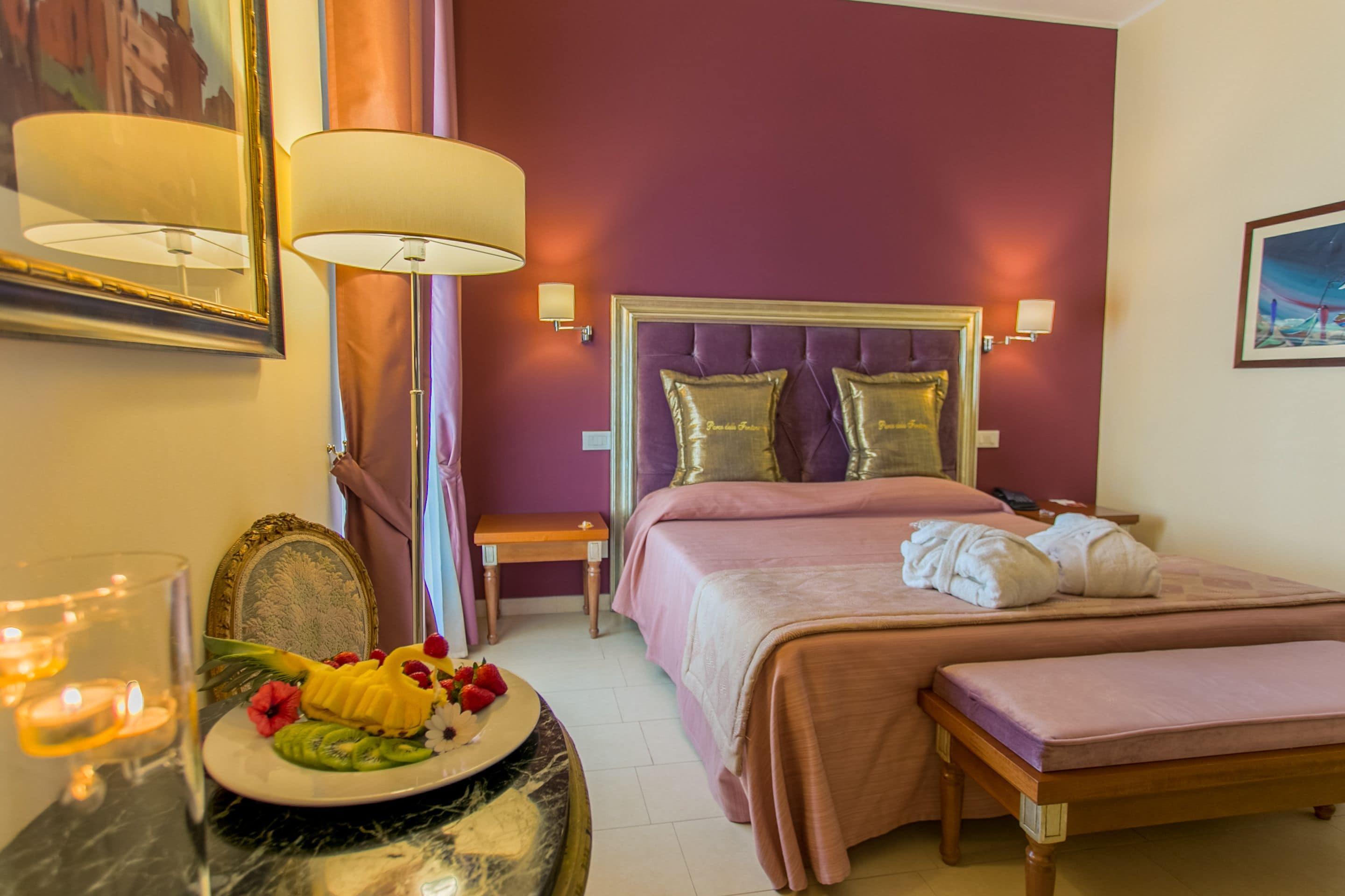 A hotel room with a bed, bedside tables, a mirror, and a decorative plate with fruits.