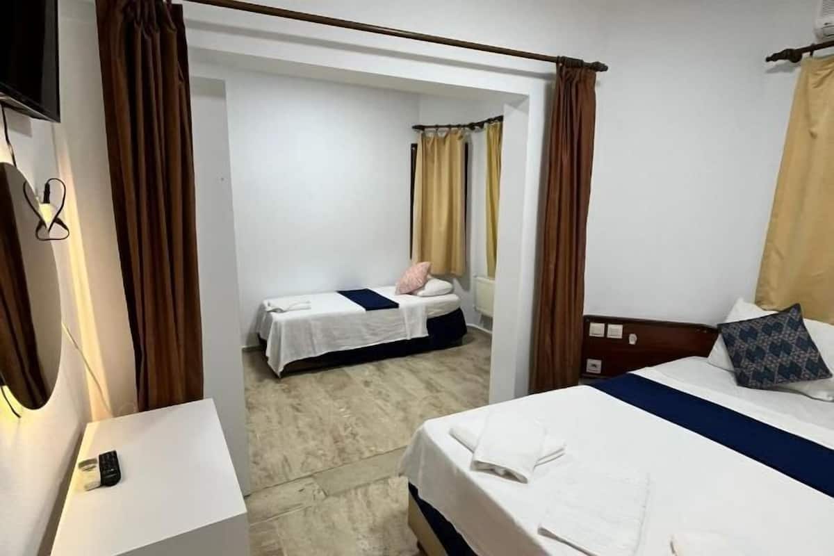 A hotel room with two beds, a small table, a remote control, and a bathroom visible through an open door.