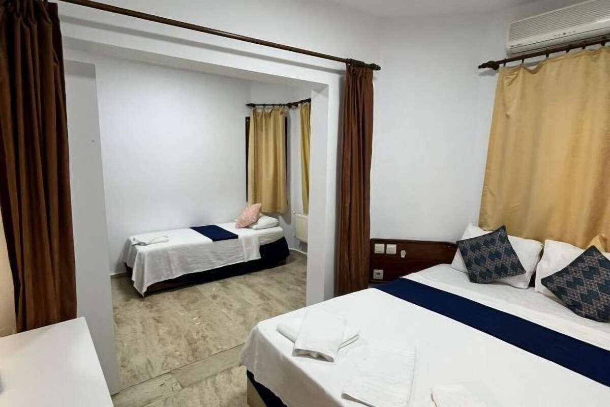A hotel room with two beds, a wooden headboard, a white wall, and a window with curtains.