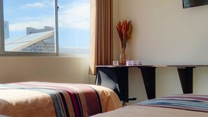 A hotel room with two beds, a desk with a computer, a TV on the wall, and a window with a view of buildings. - Hotel Sagarnaga (La Paz)