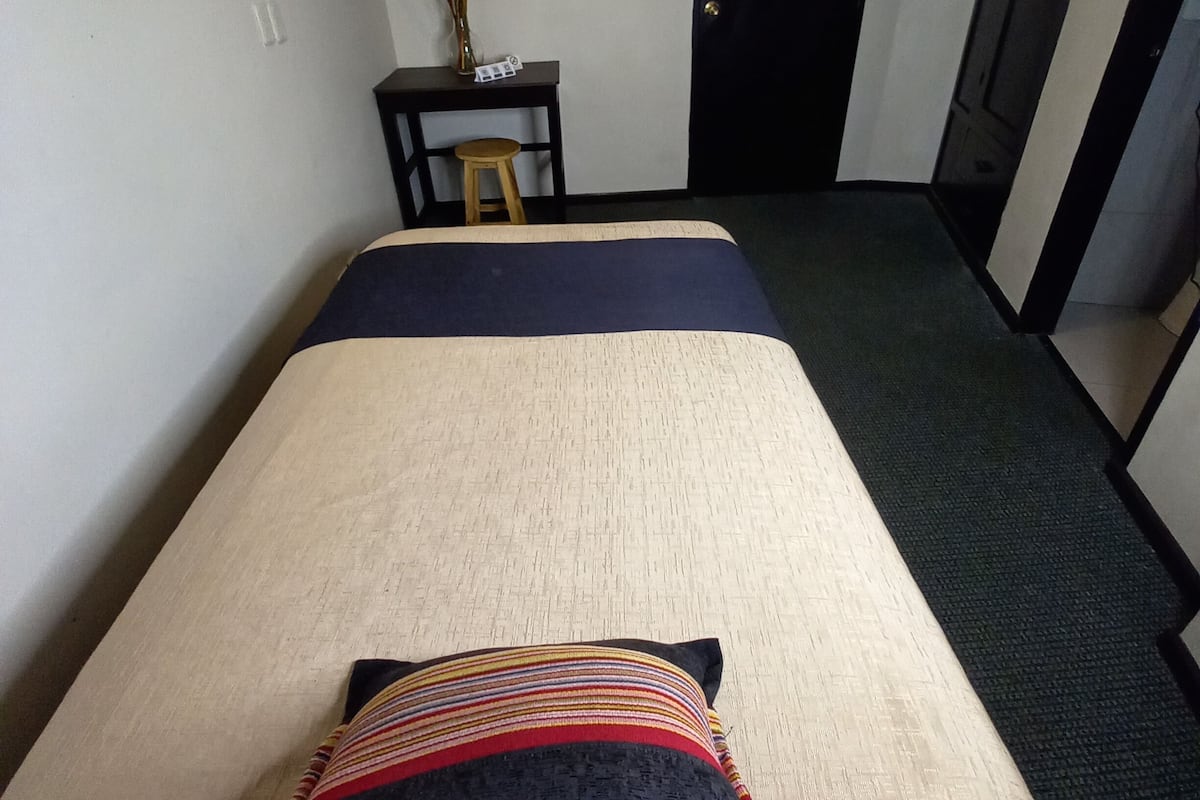 A hotel room with a bed, a desk with a vase, and a door.