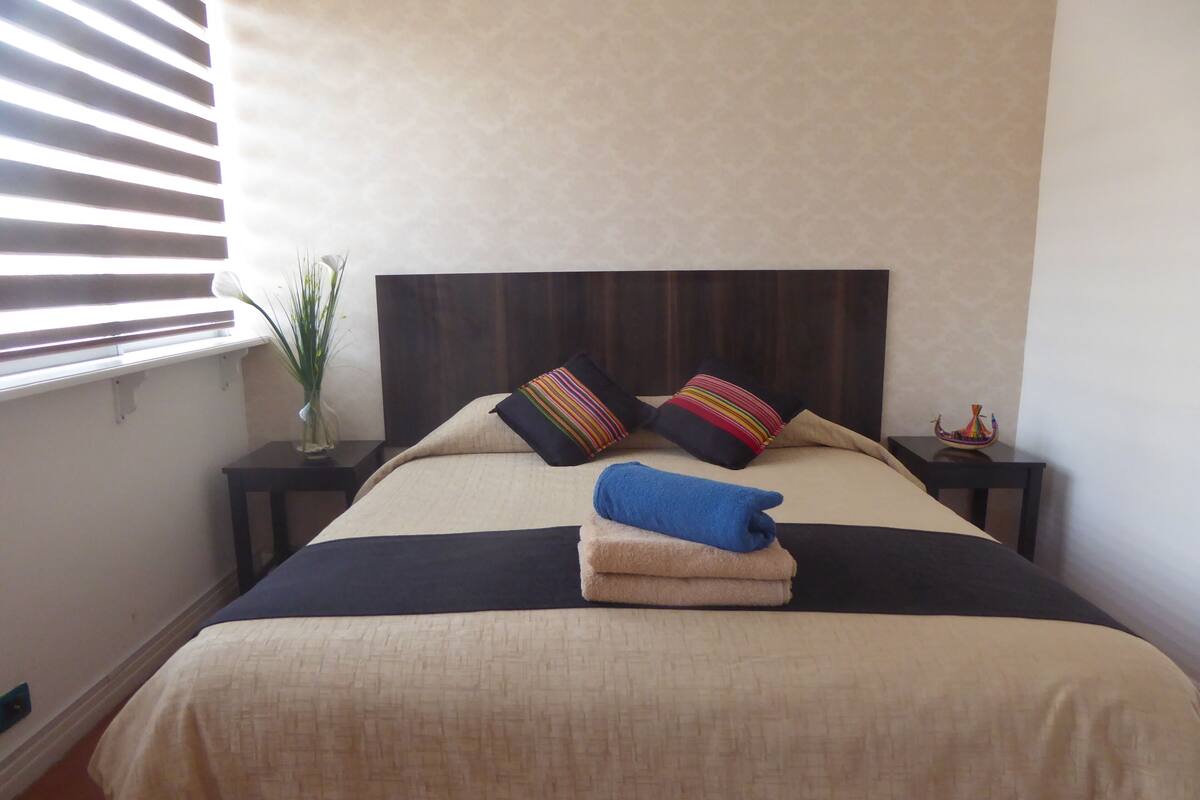 A neatly made bed with a beige and black bedspread, two colorful striped pillows, and a blue towel on the bed.