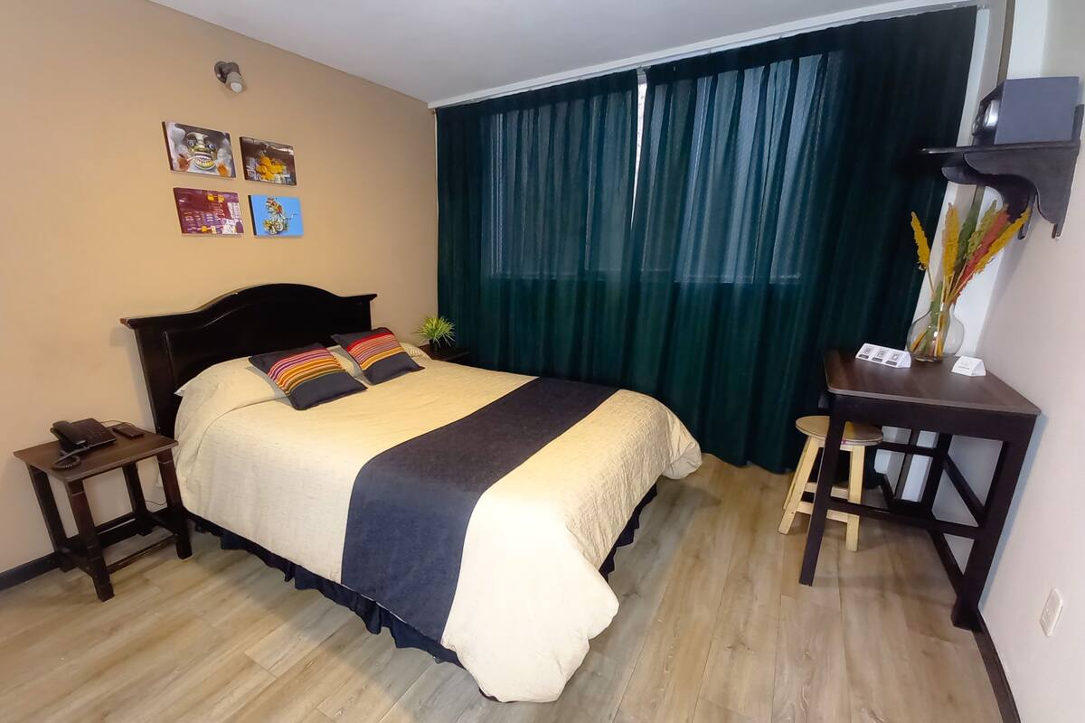 A neatly arranged bedroom with a bed, bedside tables, a desk, and a curtain.