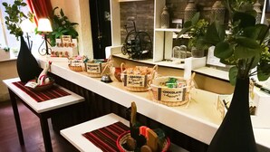 A counter with baskets labeled with food items and prices, a lamp, and decorative plants. - Hotel Sagarnaga (La Paz)