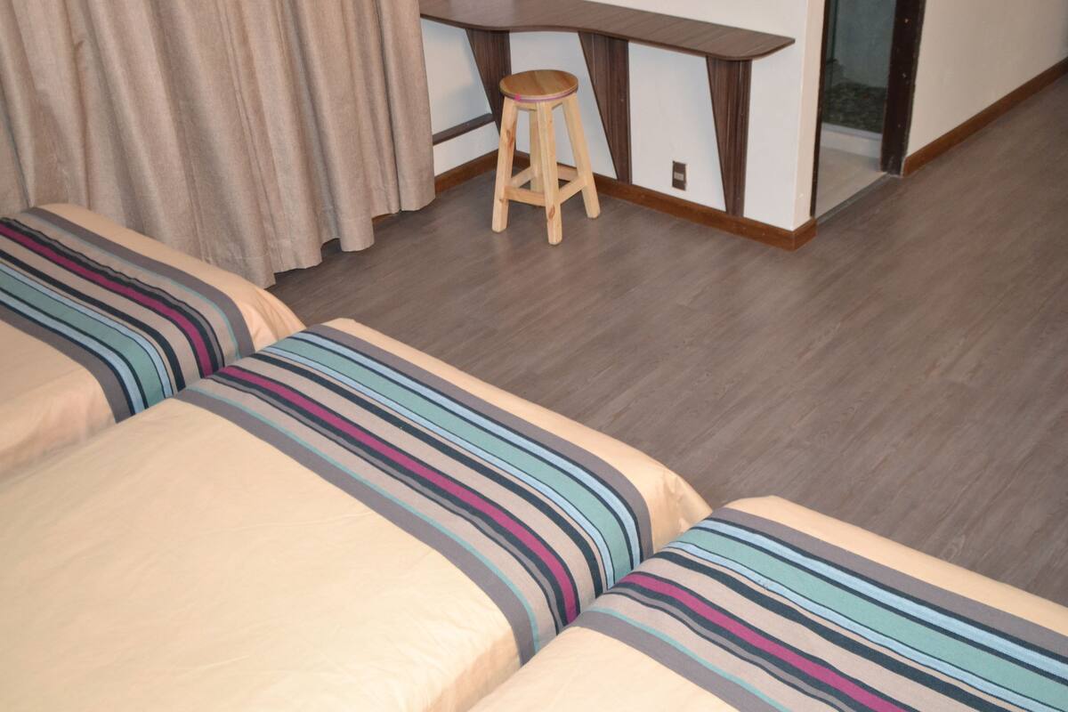 A hotel room with a large bed, a wooden stool, and a desk.