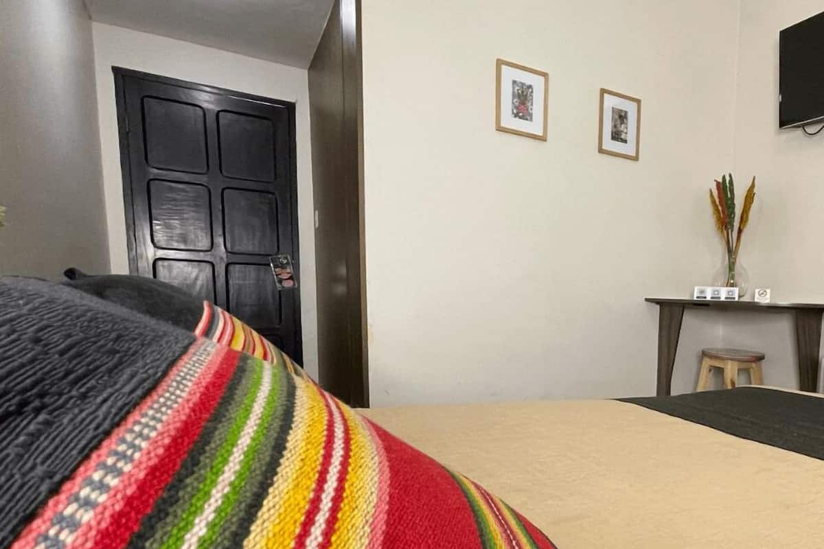 A hotel room with a bed, a desk, and two framed pictures on the wall.