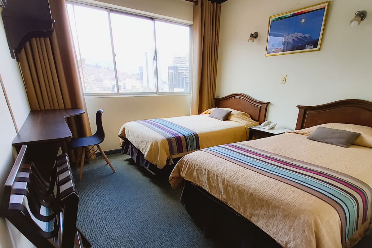 A hotel room with two beds, a desk, and a chair.