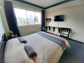 Habitación de hotel con una cama grande, un televisor montado en la pared y una ventana con vistas a la ciudad.