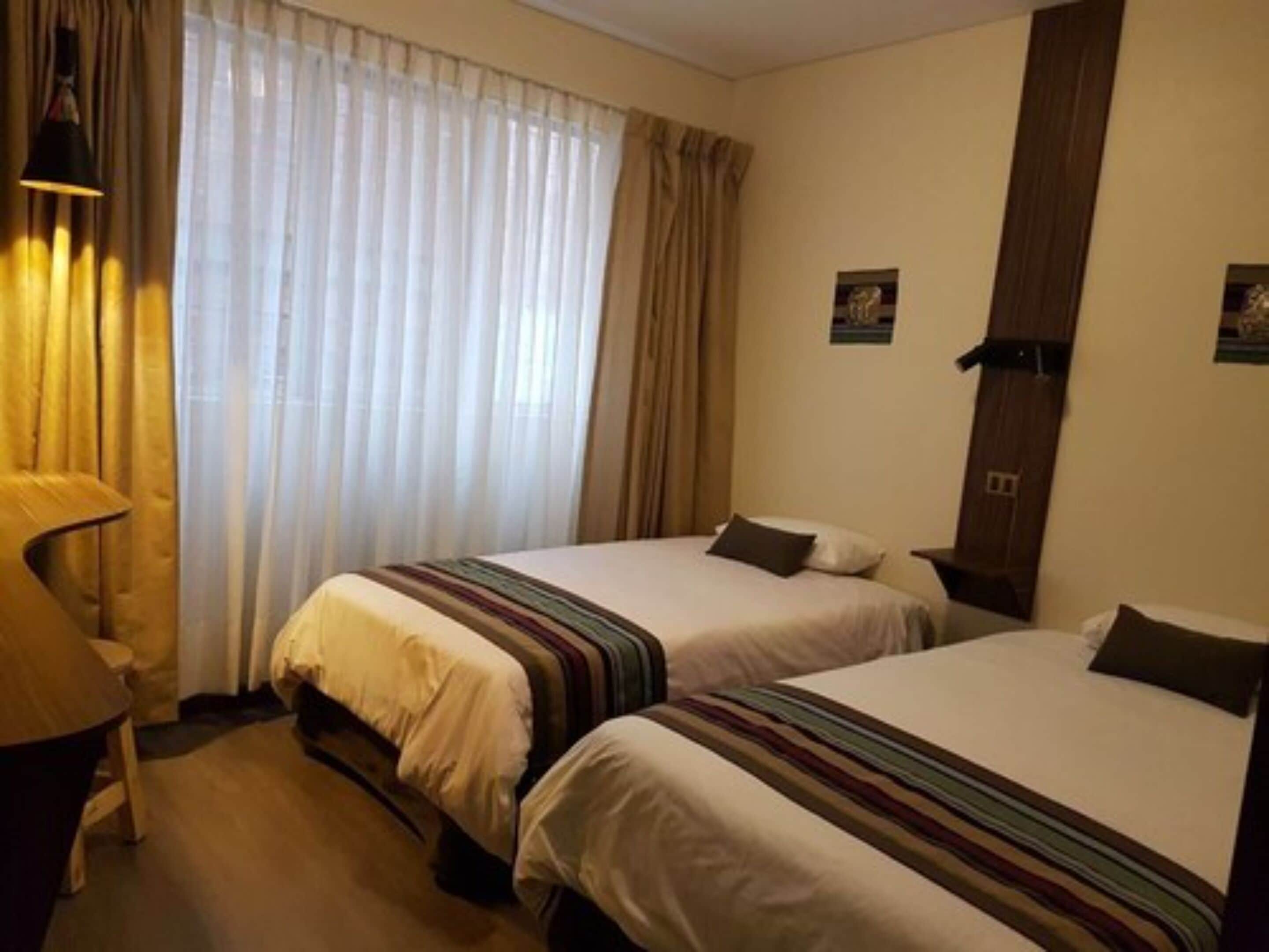 A hotel room with two beds, a desk, and a window with curtains.