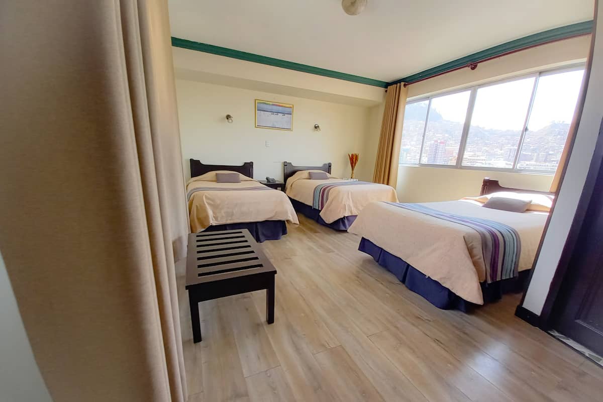 A hotel room with two beds, a small table, and a window with a city view.