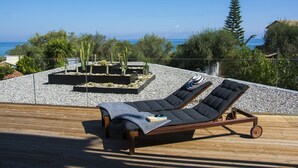 A sun lounger on a wooden deck with a view of the sea and a cactus garden.
