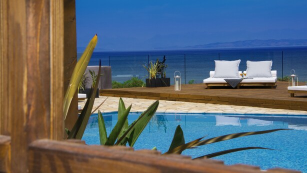 A poolside area with a view of the sea, two white lounge chairs, and a wooden deck.