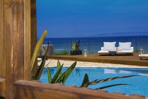 Un espace aménagé au bord de la piscine, avec vue sur la mer, comprenant deux chaises longues blanches et une terrasse en bois.