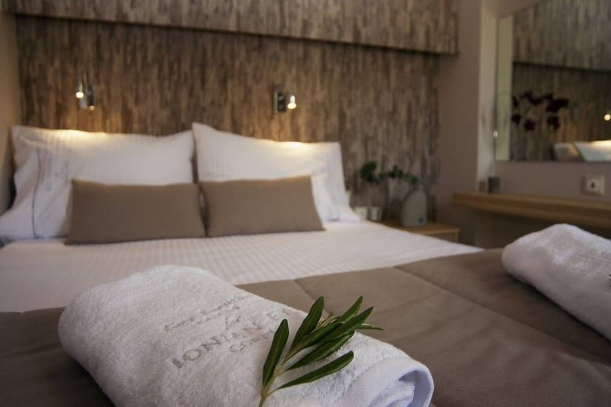 A neatly made bed with a white towel and a sprig of rosemary on it, a wooden headboard, and a bedside table with a lamp.