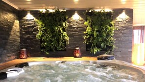 A hot tub with a stone wall and hanging plants, two decorative lanterns, and a wooden bench.