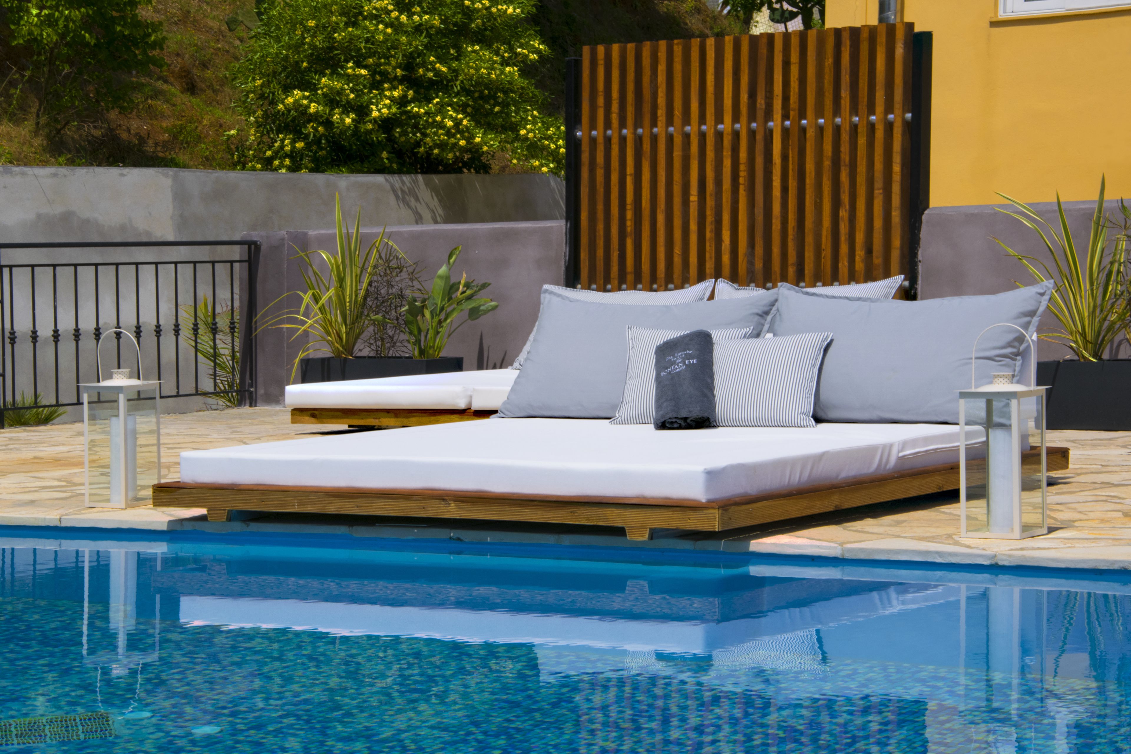 A poolside bed with a wooden frame, grey bedding, and two pillows.