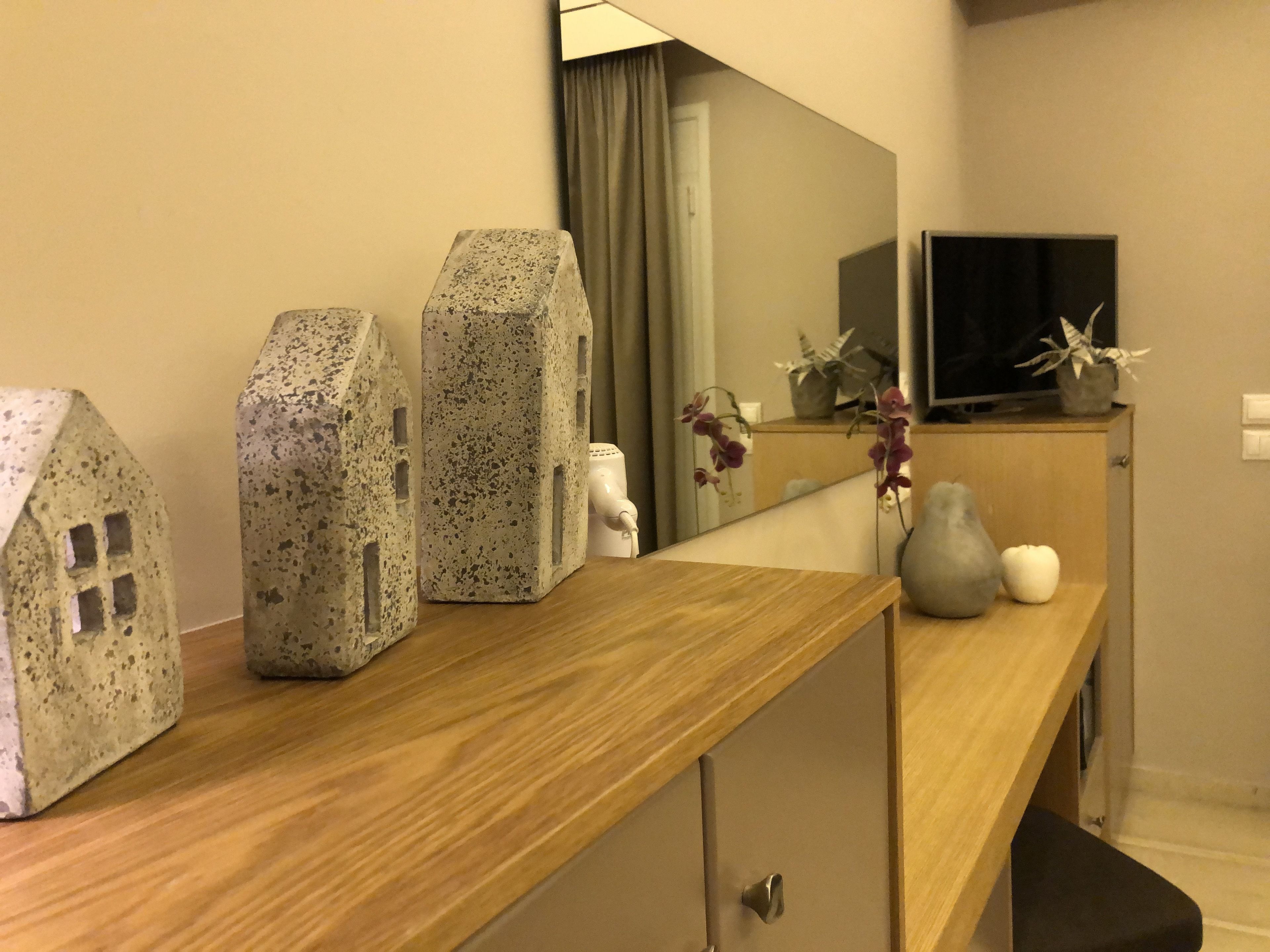 Une chambre d’hôtel avec un bureau en bois, un miroir et des objets décoratifs, notamment des vases en forme de maison et un vase avec des fleurs.