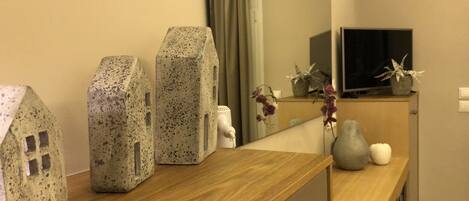 Ein Hotelzimmer mit einem Holztisch, einem Spiegel und Dekorationselementen, darunter hausförmige Vasen und eine Vase mit Blumen.
