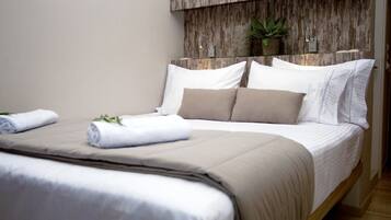 A neatly made bed with white and beige bedding, a wooden headboard, and a small potted plant on the wall.