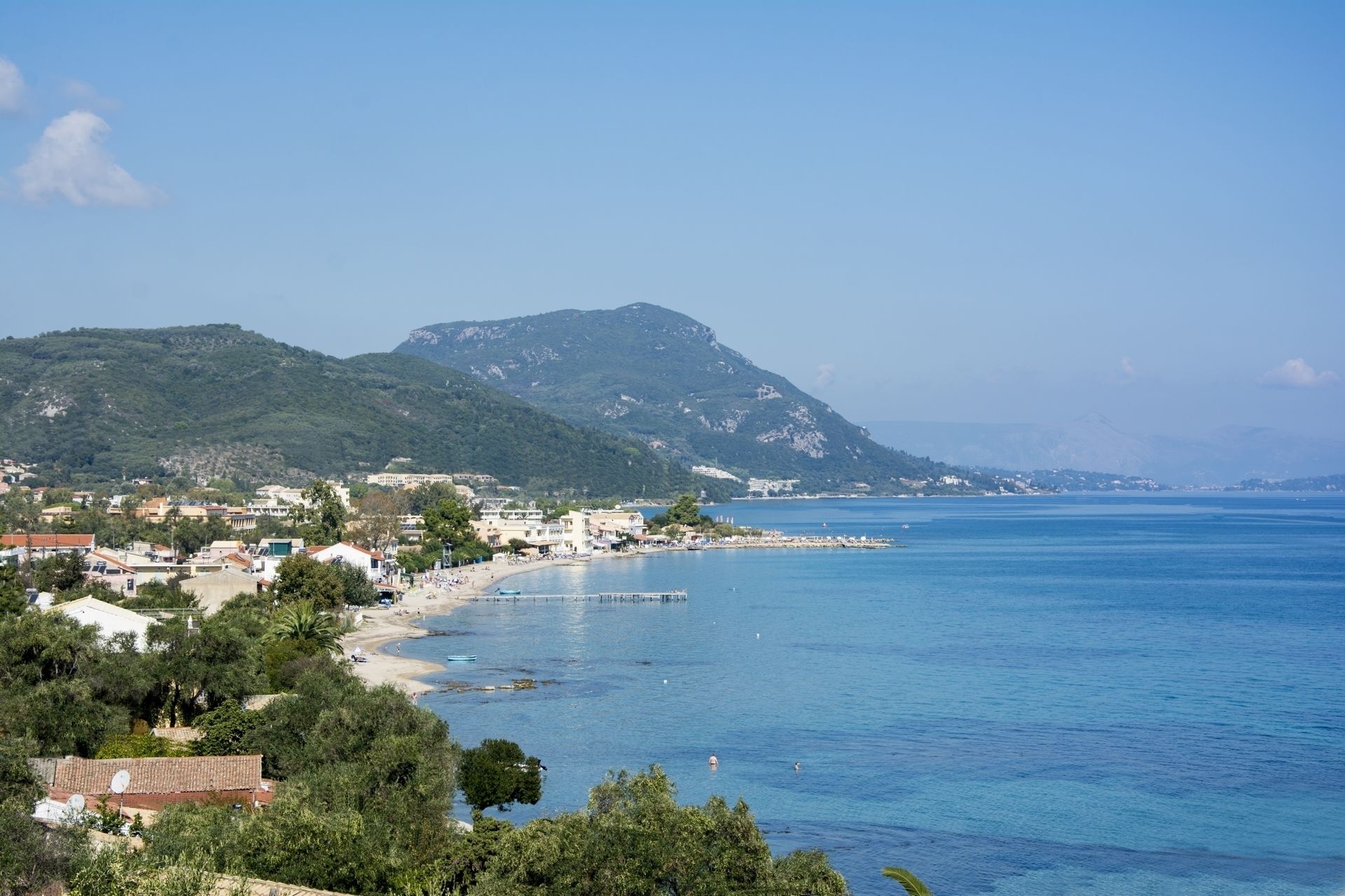 A coastal town with a beach, buildings, and a mountain in the background.
