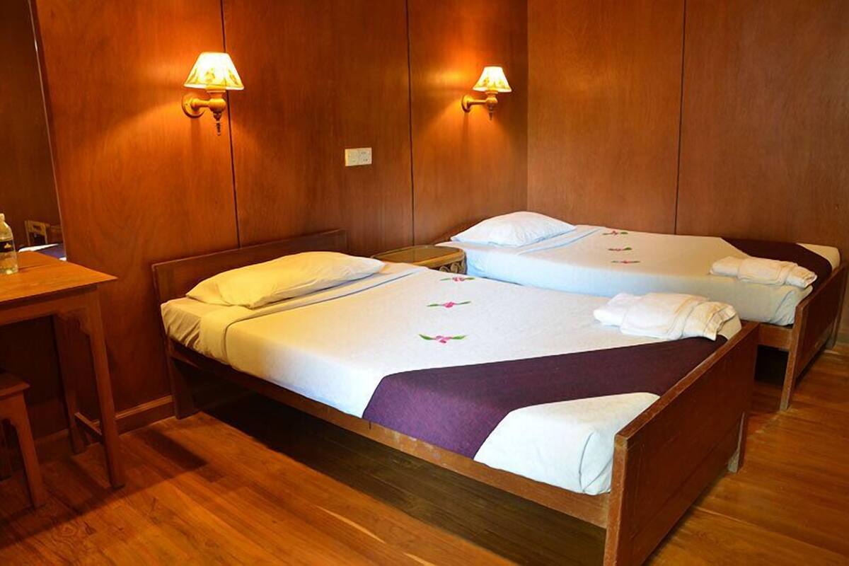 Ein Hotelzimmer mit zwei Holzbetten, jeweils mit weißer Bettdecke und violetter Decke. An jeder Seite der Betten befinden sich zwei Wandlampen.