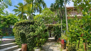 A stone pathway leading to a pool, surrounded by lush greenery and palm trees. - Rock Villa Hoi An (Da Nang)