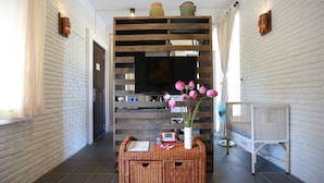 A hallway with a white brick wall, a wooden partition with a flat-screen TV, wicker furniture, and a vase with flowers. - Rock Villa Hoi An (Da Nang)