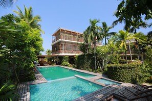 A pool area with a wooden deck, surrounded by lush greenery and palm trees. - Rock Villa Hoi An (Da Nang)