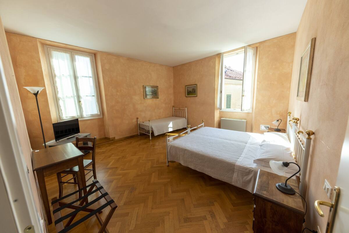 A bedroom with a bed, a desk, a chair, a radiator, and two windows.