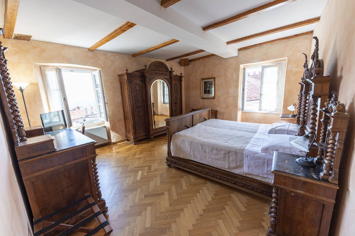 A bedroom with a large bed, wooden furniture, and a herringbone-patterned floor.