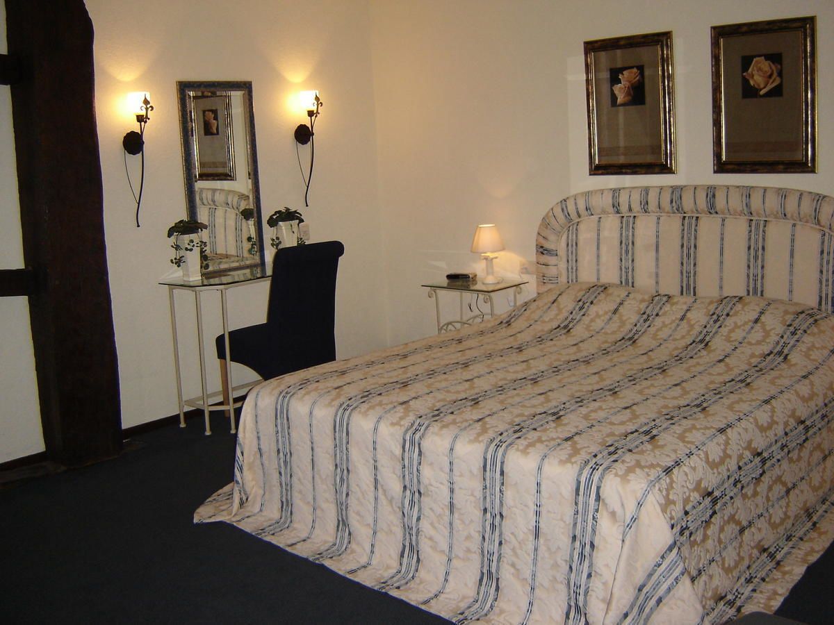 Un dormitorio con una cama grande, un escritorio con silla, dos lámparas fijadas a la pared y dos cuadros enmarcados.