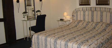A bedroom with a large bed, a desk with a chair, two wall-mounted lamps, and two framed pictures.