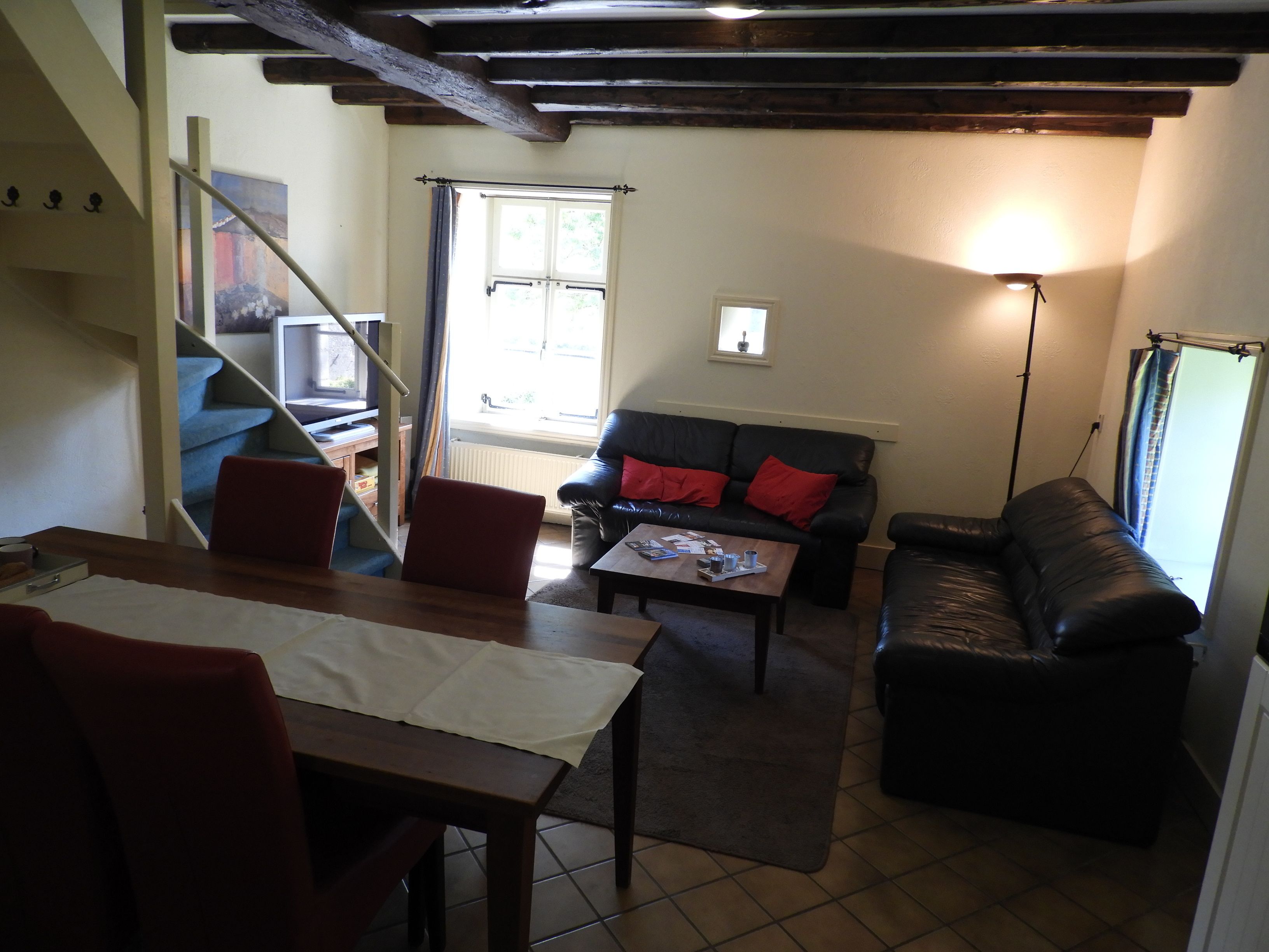 A cozy living room with a staircase, a black leather sofa, a wooden coffee table, and a dining area with a table and chairs.