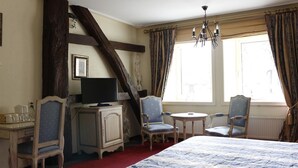A hotel room with a large bed, two chairs, a small table, a television, and a window with curtains. - Kasteel Schaloen (Schin op Geul)