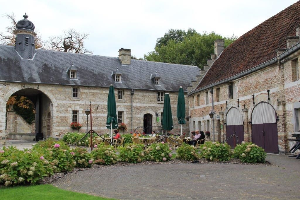 A courtyard with stone buildings, outdoor seating, and green umbrellas.