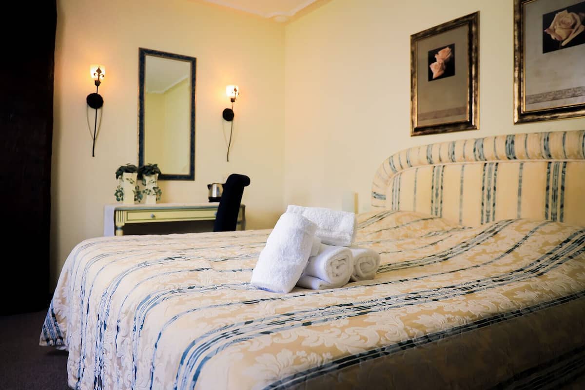 A neatly made bed with a striped headboard, a bedside table with a lamp, and a mirror on the wall.
